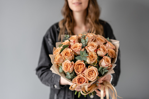 Portrait of a beautiful young woman holding a bouquet of orange color roses, studio shot in front of a white background