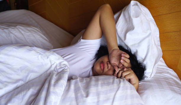 istock Asian woman wearing white T shirt sleeping on the white bed with her hands on her head 1162497607