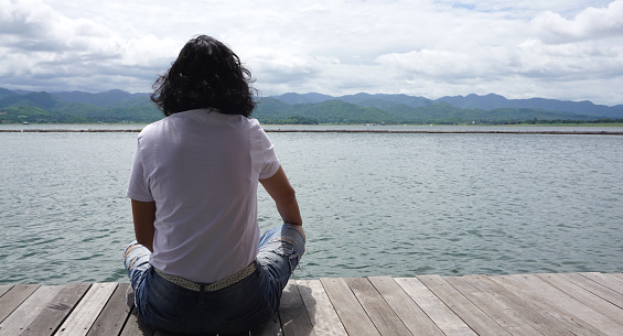 Asian woman wearing white T shirt and jean sitting on the timber deck out door with beautiful lake and mountain view