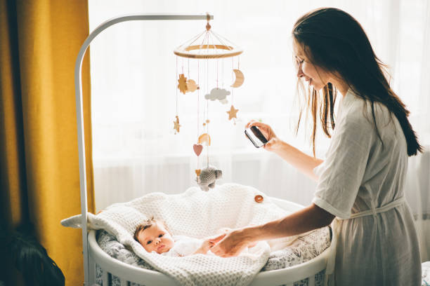Mother taking a picture Mother taking a picture of A baby with a mobile phone. Mother holding daughter hand and smiling. Mother standing near the cradle and holding baby's hand. Concept photo parenthood and motherhood. crib photos stock pictures, royalty-free photos & images