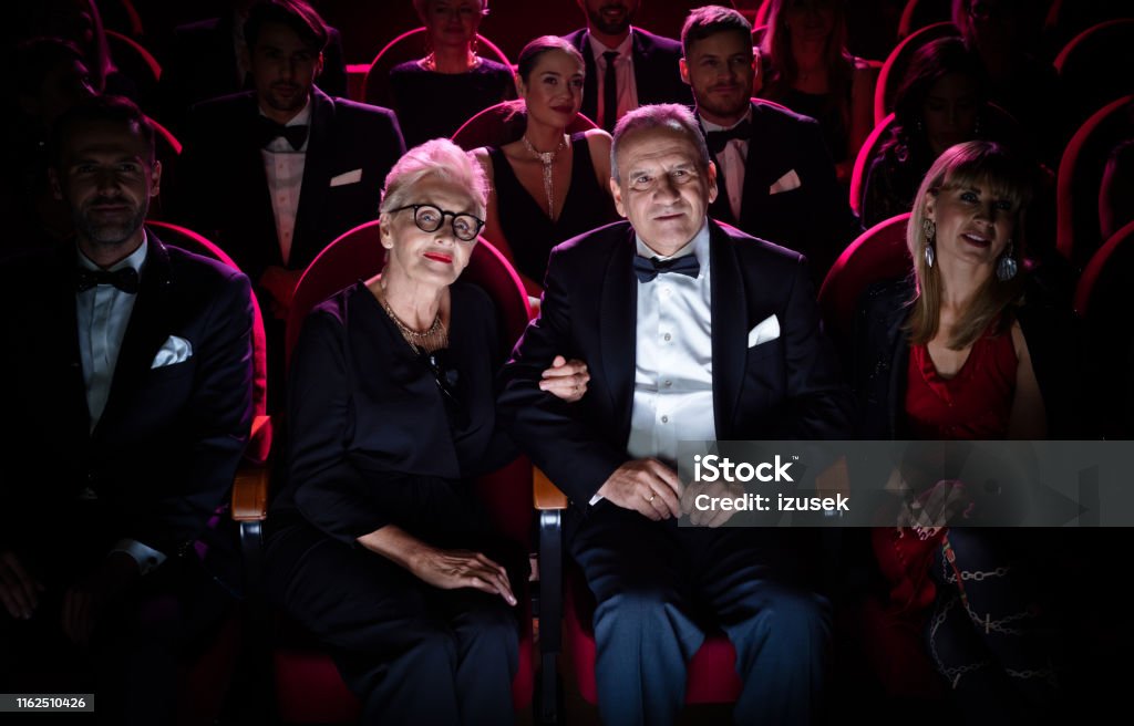 Senior couple watching theatrical performance Senior couple watching theatrical performance. Man and woman are sitting between crowd in theater. They are dating during weekend. Opera Stock Photo