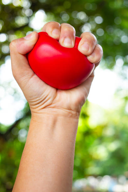 istock Woman's left hand squeezing red stress ball on bokeh green garden background, Exercise and Massage concept 1162513831