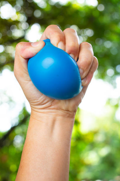 istock Woman's left hand squeezing blue stress ball on bokeh green garden background, Exercise and Massage concept 1162513836