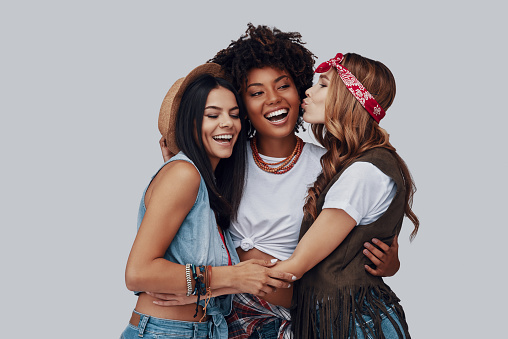 Three attractive stylish young women embracing and laughing while standing against grey background