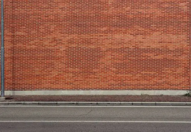 Photo of High brick wall with a porphyry sidewalk and an asphalt street in front. Urban background