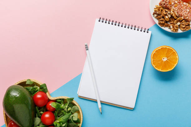 istock top view of empty notebook, vegetable salad, orange and nuts on pink and blue background 1162531010