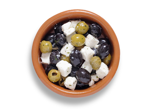Green and black olives with cubes of feta cheese in a small brown bowl, shot from above isolated on white with path