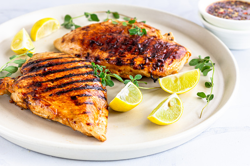 Grilled Chicken Breast with Fresh Herb and Lemon  Directly Above Photo. Cooked Chicken Breast in a White Plate \