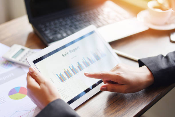 istock Business woman working in office with checking business report using tablet computer technology laptop with calculator and coffee cup - Sale report money analyzing graphs chart 1162542282