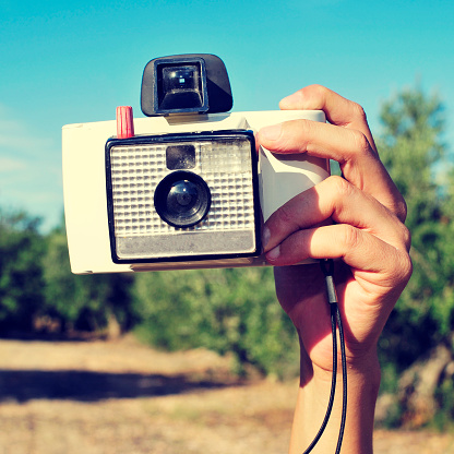 closeup of the hand of a young man taking a picture with an old instant camera, in a natural scenery, with a retro effect
