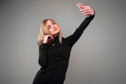 blonde woman taking selfie in studio on gray background