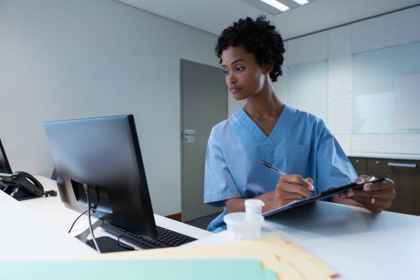 Female surgeon writing on clipboard while working on computer at desk