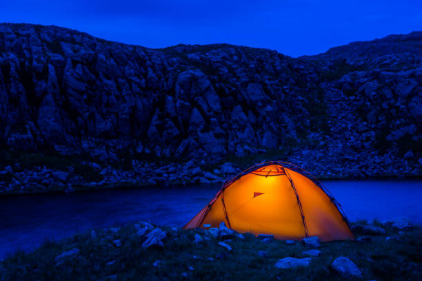istock Warmly illuminated mountain tent at night camping beside wilderness lake 1162547606