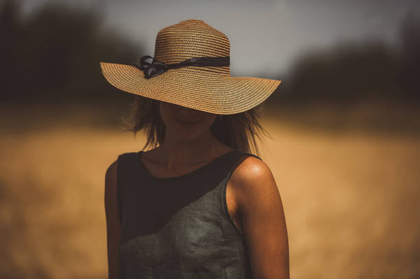 Young woman on field hiding her eyes below her hat. Closeup portrait