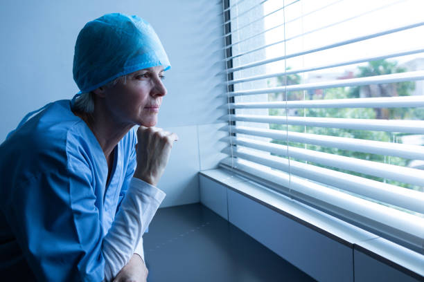 istock Female surgeon looking through window blinds in the hospital 1162551433