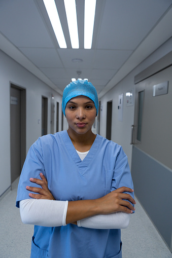 Portrait of Mixed race female surgeon standing with arms crossed while looking camera in the corridor at hospital. Shot in real medical hospital with doctors nurses and surgeons in authentic setting