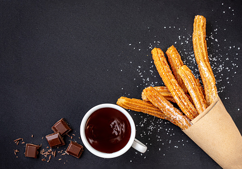 Churros with liquid chocolate. Churro - Fried dough pastry with sugar powder isolated on black stone background. Copy space