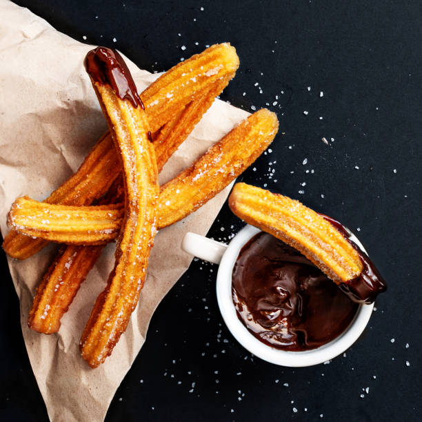 istock Churros with sugar dipped in chocolate sauce on a black background. Churro sticks. Fried dough pastry, top view 1162551962