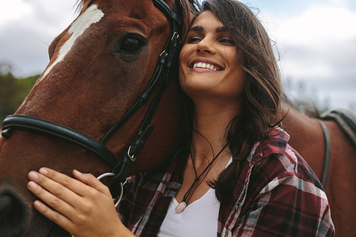 Close up of happy young woman hugging her horse. Cowgirl loving her horse outdoors.