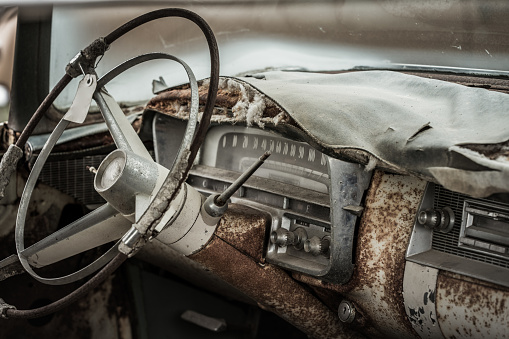 Interior with dashboard and instrumentation from an abandoned and very worn, beat up classic car from the fifties