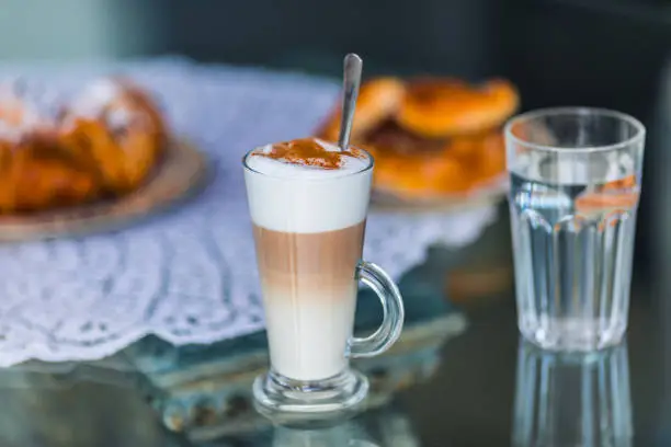 Coffee latte in glass with milk foam and cocoa, cinnamon powder and cake bisquit for breakfast