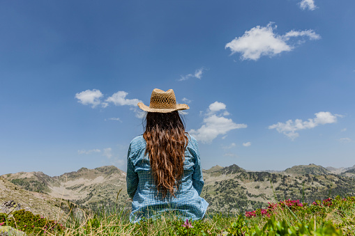 Woman with straw hat sits between alpine roses in mountains