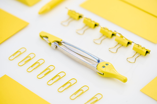 selective focus of yellow paper clips, compasses and envelope on white background