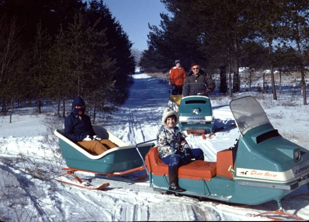 Wyoming, United States - January 01, 1976:  Vintage, authentic archival photograph of a family wearing heavy winter coats and smiling while posing outdoors on a snowmobile in Wyoming, United States, 1976