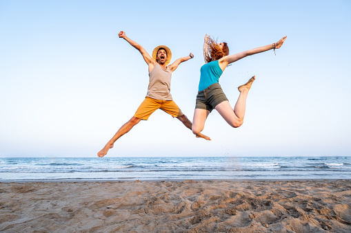 Young couple having a ball jumping on the seashore at sunset in a Mediterranean beach.