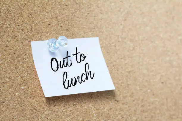 Out to lunch handwriting note on a wooden corkboard