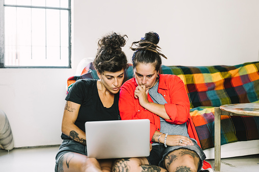 Two woman sitting on a floor, looking at laptop.