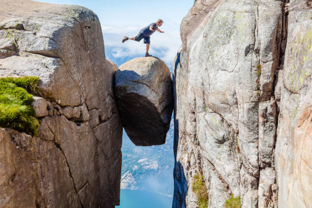 wanderer balanciert auf kjeragbolten über lyseford in norwegen - kjeragbolten stock-fotos und bilder