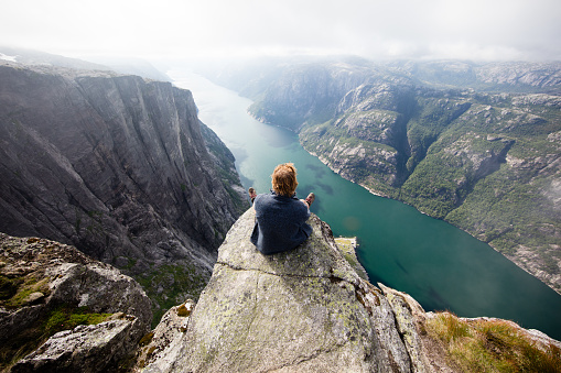 Hiker sitting on Kjeragnasen over Lyseford in Norway