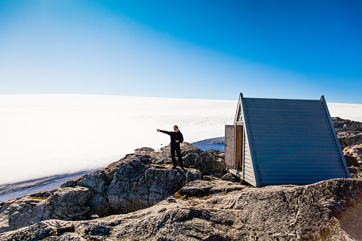 Hiker standing in front of Small hut at Folgefonn glacier in Norway pointing at something