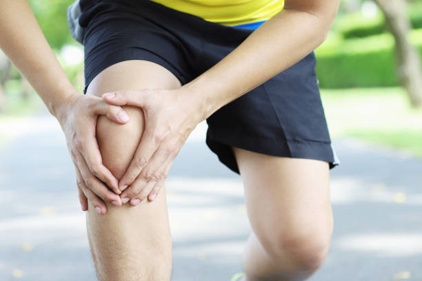 corridore che tocca dolorosa caviglia attorcigliata o rotta. incidente di allenamento dell'atleta corridore. la distorsione alla caviglia che corre sportiva causa un infortunio al ginocchio. e dolore alle ossa delle gambe. colore rosso focus gambe su per m - human knee physical injury bandage muscular build foto e immagini stock