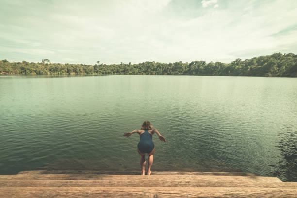 frau springt in das wasser des vulkanischen sees umgeben von wald in banlung, kambodscha, reiseziel. getönte vintage-stil - den sprung wagen fotos stock-fotos und bilder