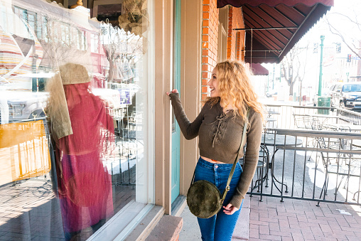 This is a photograph of a young 18 year old Hispanic woman with long curly blonde hair window shopping along a Main Street in Arvada, Colorado, a Denver suburb.