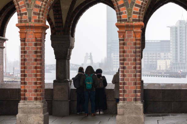 People standing under the Oberbaum Bridge in Berlin, Germany. The Oberbaum Bridge is a double-deck bridge crossing Berlin's River Spree, considered one of the city's landmarks. It links Friedrichshain and Kreuzberg, former boroughs that were divided by the Berlin Wall, and has become an important symbol of Berlin’s unity. The upper deck of the bridge carries Berlin U-Bahn lines U1 and U3, between Schlesisches Tor and Warschauer Straße stations.