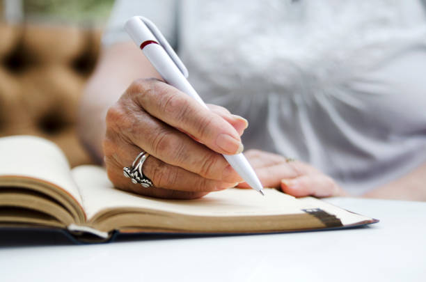mujer mayor escribiendo con lápiz en el libro de notas abierto. - diary writing women human hand fotografías e imágenes de stock
