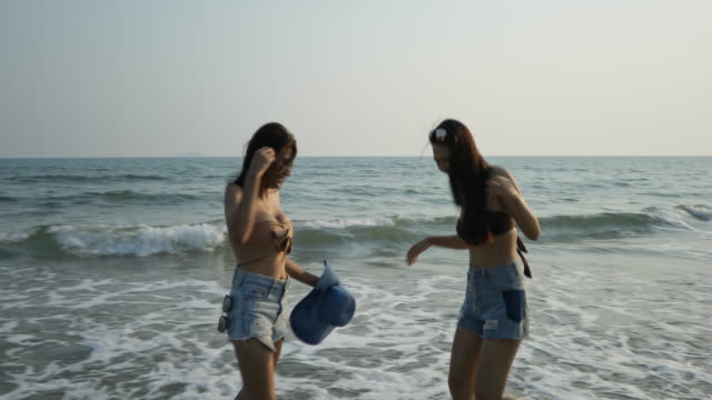 Asian teenage girls dancing playfully tease each other on the beach with beautiful sea in Thailand.