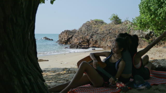 The Asian teen girl playing guitar and singing, having fun on the beach with beautiful sea in Thailand.