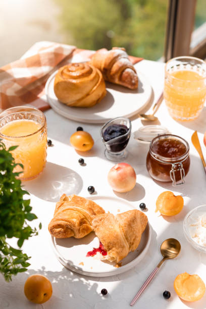 kontinentales frühstück mit orangensaft, croissants, marmelade und früchten auf dem tisch am fenster mit sonnenlicht - pension altersvorsorge stock-fotos und bilder