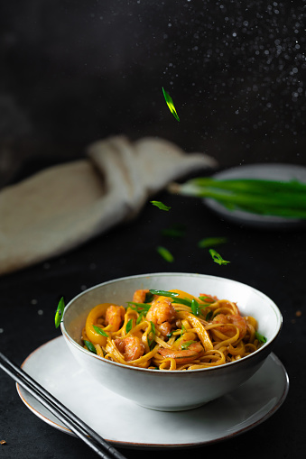 Stir fry udon noodles, shrimps, leek and vegetables. Asian healthy food in bowl over black background, copy space.
