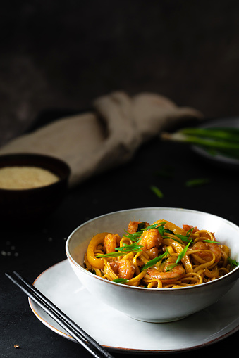 Udon stir-fry noodles with shrimp and vegetables on black background in dark and moody style