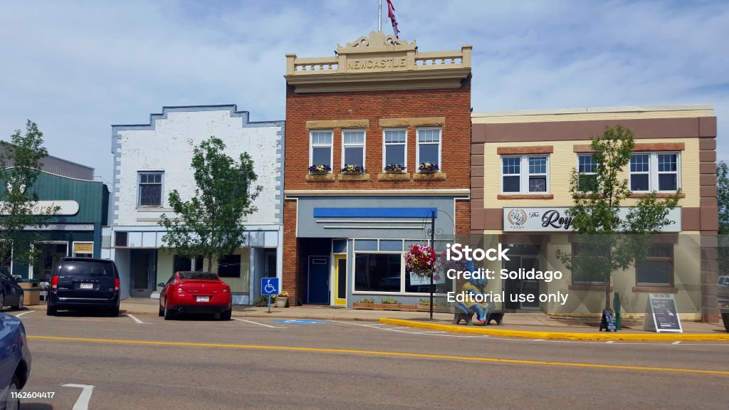 Small Town Alberta Downtown Drumheller Heritage Buildings Drumheller,Alberta, Canada- July 10,2019: Main Street downtown Drumheller. Restored and Refurbished old heritage buildings. Female Dinosaur sitting on bench. Cars parked. Small Town America Stock Photo