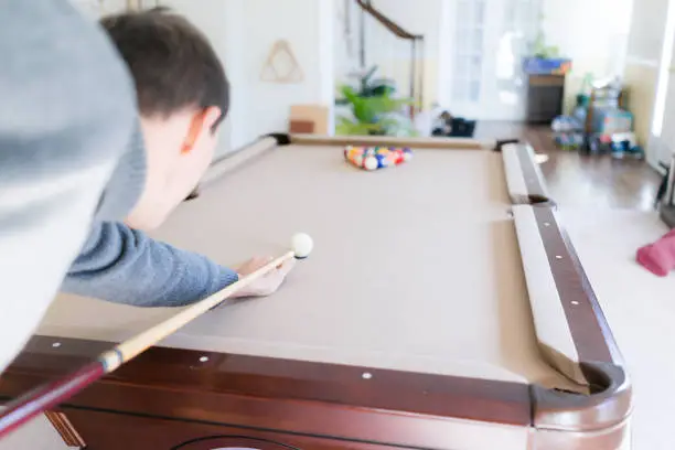 Interior inside house home with billiard pool table in living room, young man in winter cold sweater shooting white ball during game start with cue