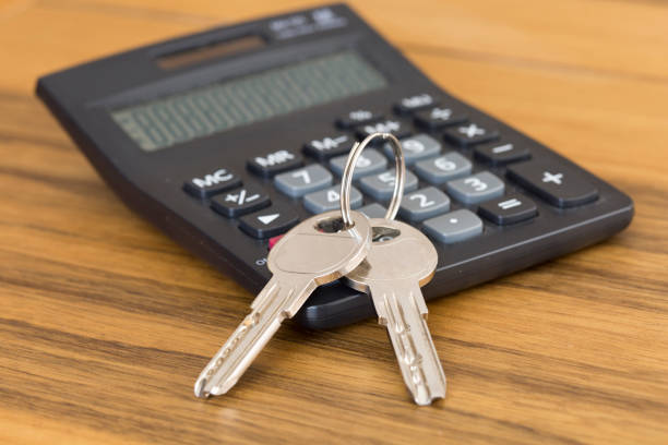 istock Calculator with a house key. Background with wooden table. 1162606854