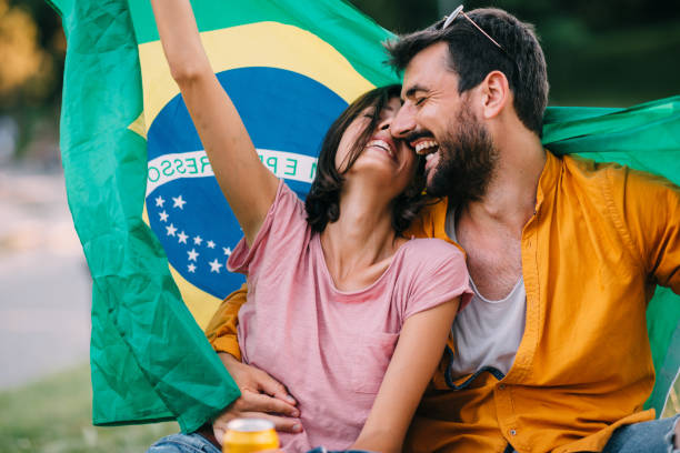 Joven pareja bailando en un festival en el parque con bandera de Brasil - foto de stock