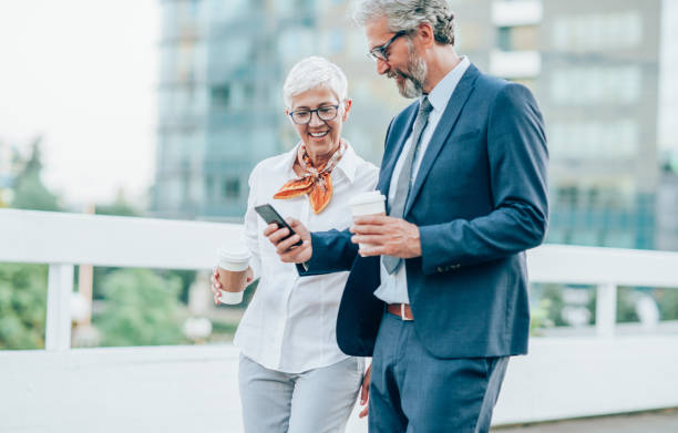 istock Two mature business persons using phone outdoors 1162615040