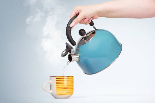 istock Female hand pours hot water from a blue kettle into a mug with a drink, on light background 1162618219